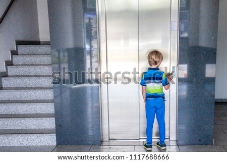 Little boy is calling the elevator next to staircase