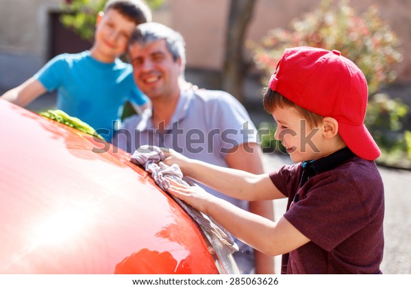 Little boy in cap washing car with dad and\
brother, fun with family