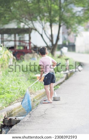 A little boy is catching fish with a fishing net at a roadside creek in the countryside