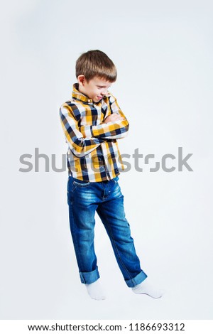 Little boy in a checked shirt on a white background folded his arms and smiles.
