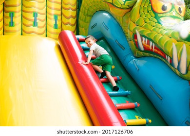 Little Boy Child Climbs The Stairs Of A Multi-colored Slide In The Park.