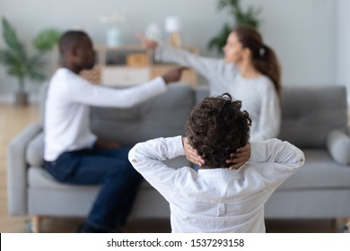 Little boy child cover ears avoid hearing multiethnic parents scream argue at home, small preschooler kid suffer from mom and dad fight dispute in living room, having psychological effect on son