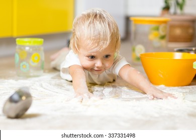 Little boy child laying on very messy kitchen floor. Toddler covered in white baking flour.