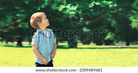 Little boy child outdoors in summer green sunny park and looking up at tree enjoying beautiful nature, blank copy space