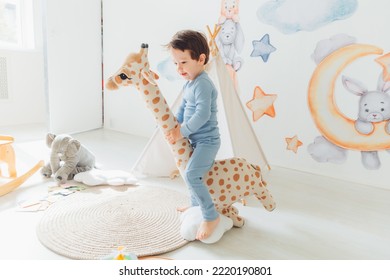 A Little Boy In A Children's Playroom With A Wigwam And A Giraffe Playing With Wooden Toys With Cubes, Child Development. Baby Rides A Giraffe Toy