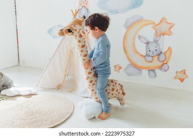 A Little Boy In A Children's Playroom With A Wigwam And A Giraffe Playing With Wooden Toys With Cubes, Child Development. Baby Rides A Giraffe Toy