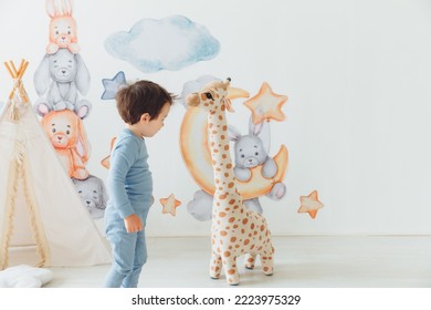 A Little Boy In A Children's Playroom With A Wigwam And A Giraffe Playing With Wooden Toys With Cubes, Child Development. Baby Rides A Giraffe Toy