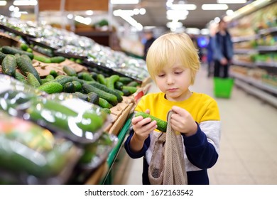 Little Boy Choosing Organic Cucumbers And Put Into Mesh Shopping Bag In Food Store Or Supermarket. Healthy Lifestyle For  Family With Kids. Concept Of Zero Waste, Recycling And Protection Environment.