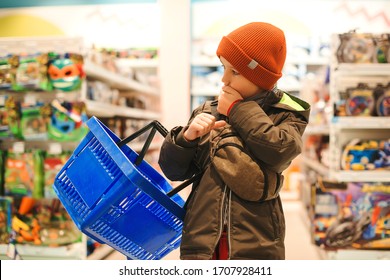 Little Boy Choosing Toy In Supermarket. Kid Difficult To Choose The Best Toy. Child With Shopping Basket At The Toys Shop. Christmas Sales. Shopping And Sales.