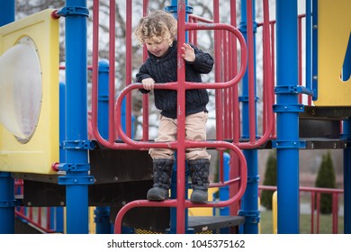 A Little Boy Is Climbing Up The Equipment At The Playground During Recess. The Child Is I Preschool, Almost Kindergarten. He Is Active And Playing Outside At The Park In His Winter Boots And Sweater. 