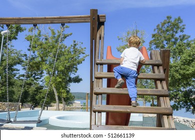 Little Boy Climbing Ladder On Slide At Playground. Child Is Facing Away, Is 4-5 Years Of Age And Caucasian