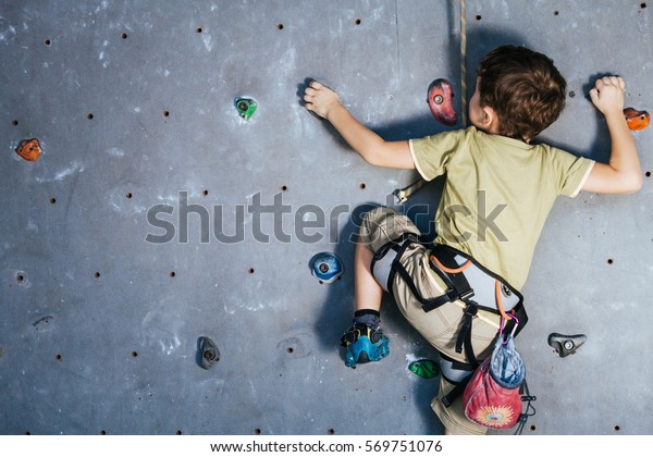 little boy climbing a rock wall indoor. Concept of\
sport life.