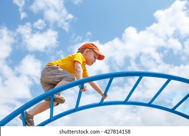 little boy climbs up the ladder on the playground. child climbs confidently up the ladder against the blue sky. copy space for your text