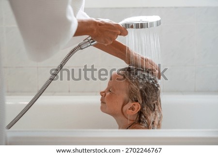 Little boy closing eyes while adult rinses shampoo foam from his