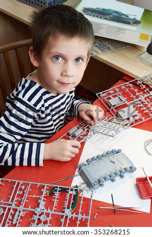 Little boy collects plastic model tank on home workplace