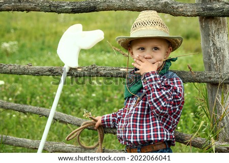 a little boy cowboy in hat with rope near fence on nature