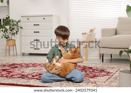 Little boy with cute ginger cat on carpet at home