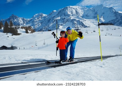 Little boy and a dad go up on the ski moving walkway belt at skiing school during winter vacations looking aside, waving hand