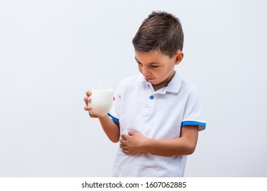 Little Boy With Dairy Allergy Holding Glass Of Milk Indoors. Child With Painful Expression After Drinking Milk. Lactose Intolerance.