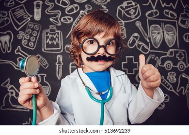 Little Boy In Doctor Costume Holding Sthetoscope And Shows Class On Dark Background With Pattern. The Child Has Mustache, Glasses