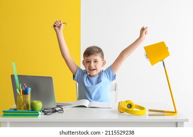 Little boy doing homework at table on color background