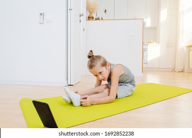 Little Boy Doing Yoga In Front Of A Laptop At Home, Stretching On A Mat. Taking Care Of Himself While Staying At Home. He's Patient, Looking Closely At Screen.