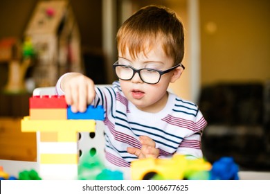 Little Boy With Down Syndrome In Black Glasses Playing With Colorful Blocks.