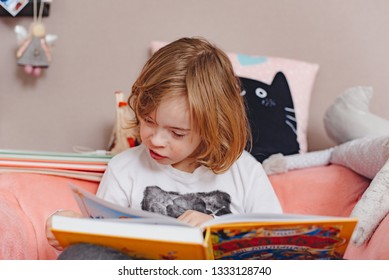 A Little Boy With Down Syndrome Is Reading A Book.