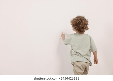 Little boy drawing on white wall indoors, back view. Space for text - Powered by Shutterstock