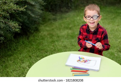 A Little Boy Drawing A Picture In The Garden (outdoors). Wearing Glasses And An Eye Patch (plaster, Occluder) To Prevent Amblyopia And Strabismus (squint, Lazy Eye). Child Vision Disease Problem.