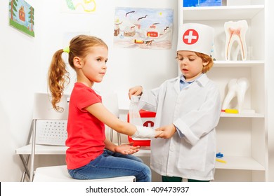 Little boy dressed like a pediatrician doctor bandaging girl's arm with a roller-bandage at the first aid room