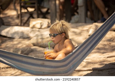 Little boy, drinking coctail, orange juice on the beack in hammock, enjoying summer. Halkidiki, Greece