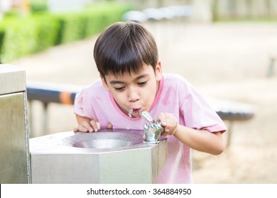 Little Boy Drinking Water In The Public Park