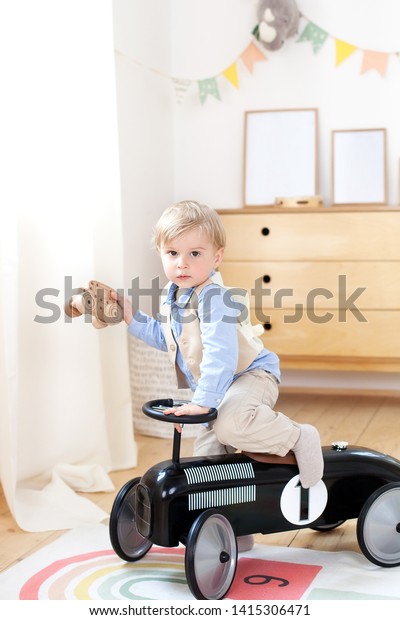 little boy driving a car pedal in the nursery. Happy\
child riding toy vintage car. Funny kid playing at home. Summer\
vacation and travel concept. Toddler driving a retro car, boy in\
toy car