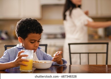 Little Boy Eating Cereal With Mom In Background