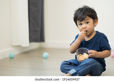 A little boy is eating cookies in the living room of the house. He is wearing a blue shirt.