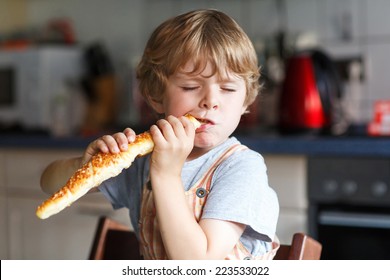 Little Boy Eating Long Loaf Bread Or Baguette In Kitchen