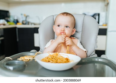 Little Boy Eating Spaghetti Look Hungry And Pasta Sauce Messes All Around His Face While Having Breakfast. Kid Boy Eats Pasta With Sauce Sitting In Kitchen