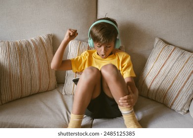 Little boy enjoying his free time using digital tablet has happy emotion and wears yellow t-shirt using green headphones. - Powered by Shutterstock