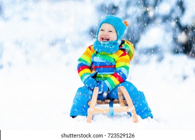 Little Boy Enjoying A Sleigh Ride. Child Sledding. Toddler Kid Riding A Sledge. Children Play Outdoors In Snow. Kids Sled In The Alps Mountains In Winter. Outdoor Fun For Family Christmas Vacation.