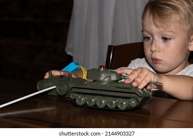 A Little Boy European German Age 3 Years Old Plays War With A Tank Model In A Dark Room On The Table.