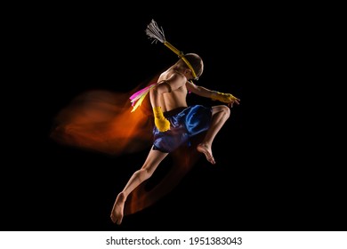 Little boy exercising thai boxing on black background. Mixed light. Fighter practicing in martial arts in action, motion. Evolution of movement, catching moment. Youth, sport, asian culture concept.
