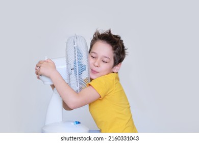 Little Boy With Fan Relaxing At Home. Summer Heat. Sunny Hot Summer Day Enjoying Fresh Air In The Front Of Working Fan.