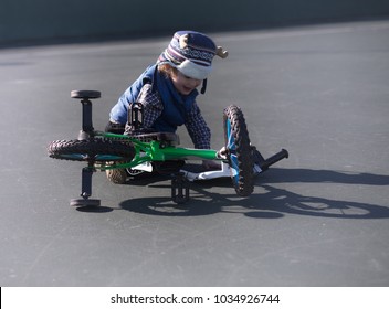 A Little Boy Feel Off His Bicycle While Riding His Bike At The Playground. The Small Child Is Learning To Ride A Bike, But Had An Accident. He Has Training Wheels. Space For Wording.