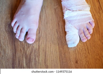 Little boy feet with injured painful left foot with white gauze bandage on thumb on brown floor background top view closeup image with copy space for text.
 - Powered by Shutterstock