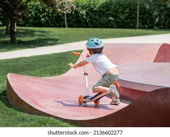 Little Boy Fell Off Kick Scooter While Riding In Skate Park. Special Concrete Bowl Structures In Urban Park. Training To Skate At Summer.