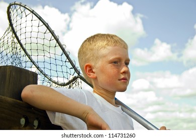 Little boy with a fishing net is leaning on a wooden dock railing