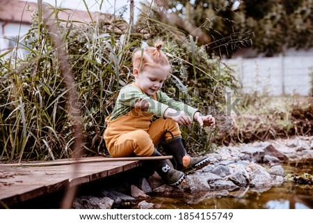 Little Boy fishing in small creek outdoors, playing in autumn day Child with a fishing rod by the water. Young fisherman relaxing and playing on a dock on lake or pond