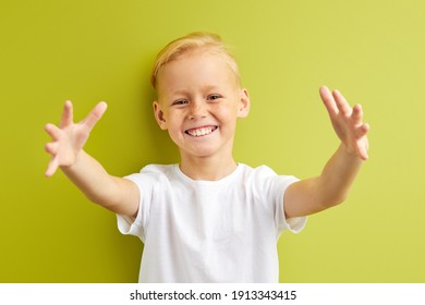 little boy with freckles spreading hands, trying to hug friend in school, positive cheerful child in casual T-shirt stand smiling at camera, isolated over green background