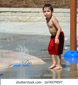 Little Boy Gets Caught With His Tongue Licking The Water From His Face At A Water Park In Arkansas.  He Is Wearing Red Swim Trunks.